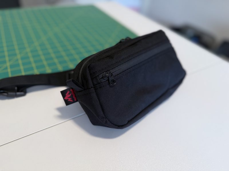 A close-up of a small black zippered bag resting on a white work surface with a cutting mat in the background.